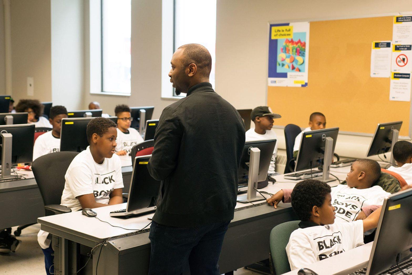 A volunteer communicating with students at a Black Boys Code Workshop