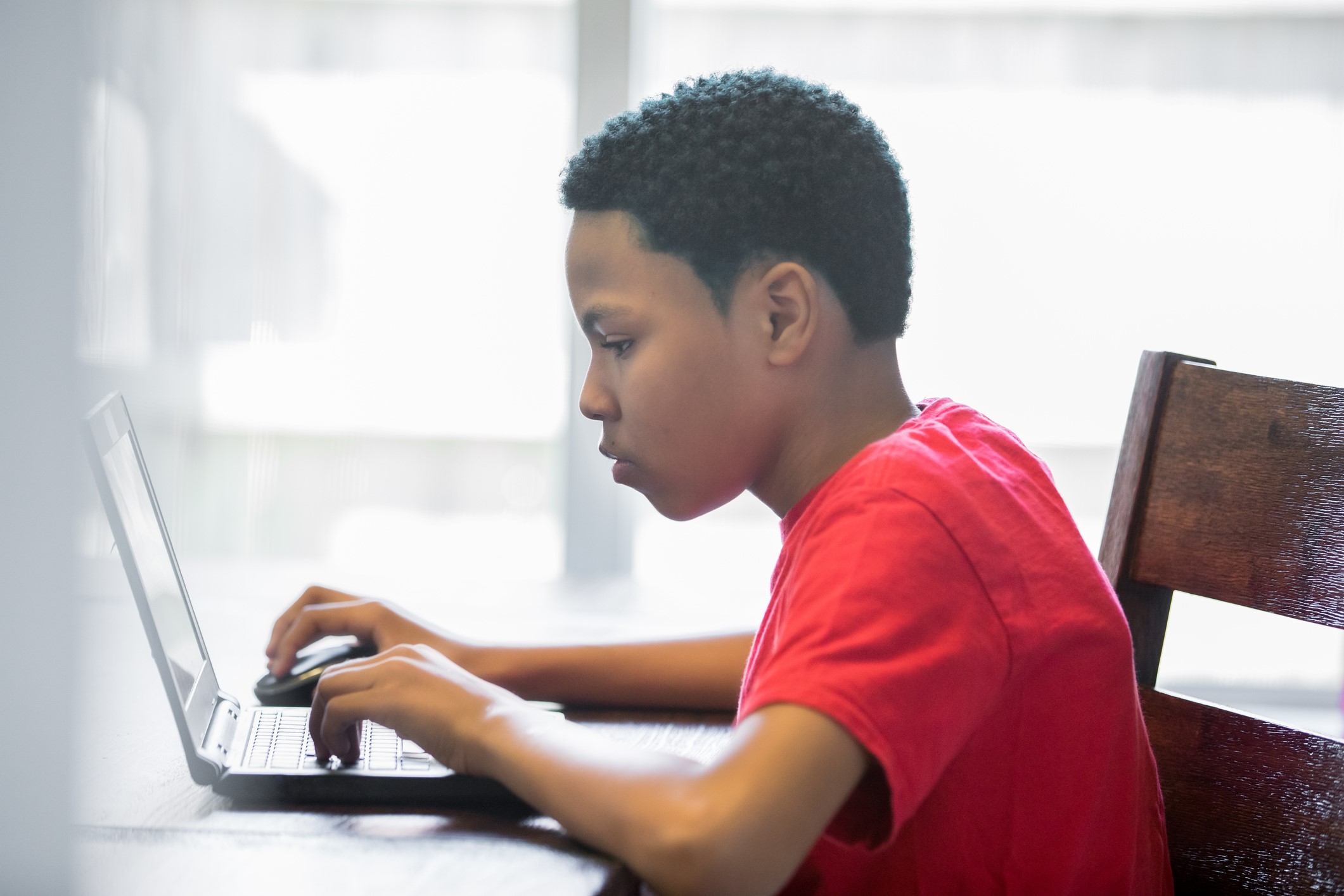 Young teenage boy working on homeschool assignments using laptop at home